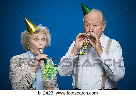 Stock Image - Older couple with noisemakers and party hats. Fotosearch