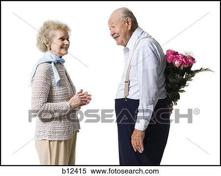 Stock Photography - Older man with bouquet of pink roses behind back. Fotosearch