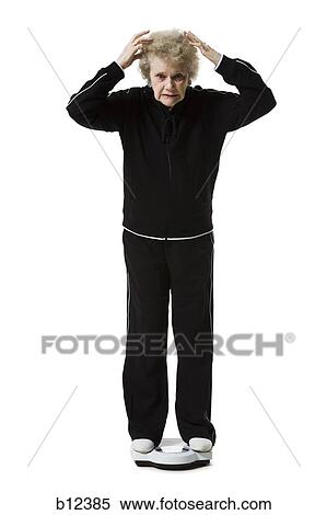 Stock Photography - Older woman weighing herself on a bathroom scale. Fotosearch