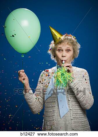 Stock Photo - Older woman with noisemaker and party hat. Fotosearch
