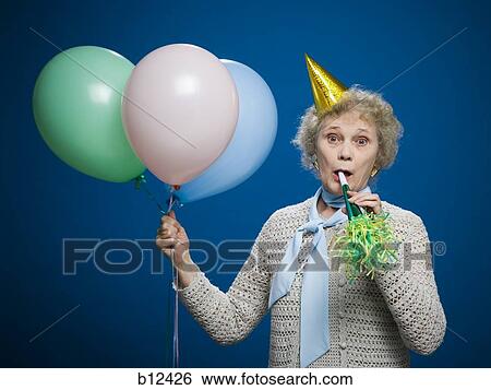 Stock Photograph - Older woman with noisemaker and party hat. Fotosearch