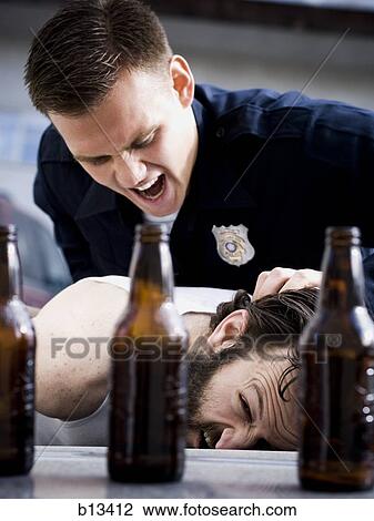 Stock Image - Police officer arresting man lying down with beer bottles. Fotosearch