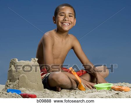 Stock Photo - Portrait of a boy sitting beside a sand castle. Fotosearch