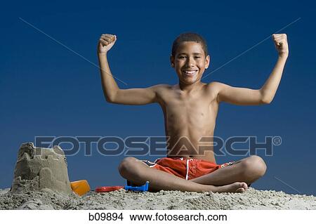 Portrait of a boy sitting near a sand castle and flexing his muscles View Large Photo Image Picture - Portrait of a boy sitting near a sand castle and flexing his muscles. Fotosearch