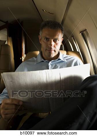 Portrait of a businessman holding a newspaper in an airplane View Large Photo Image Stock Photo - Portrait of a businessman holding a newspaper in an airplane. Fotosearch