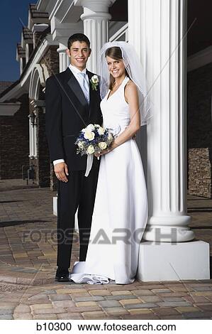 Stock Image - Portrait of a newlywed couple standing together and smiling near a column. Fotosearch