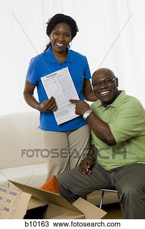 Stock Image - Portrait of a senior couple smiling and holding the deed to their new home. Fotosearch