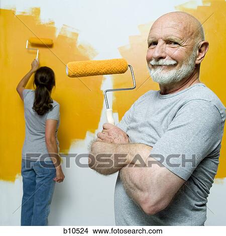 Portrait of a senior man holding a paint roller with a senior woman painting a wall View Large Photo Image Picture - Portrait of a senior man holding a paint roller with a senior woman painting a wall. Fotosearch