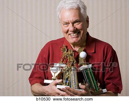 Stock Image - Portrait of a senior man holding trophies. Fotosearch