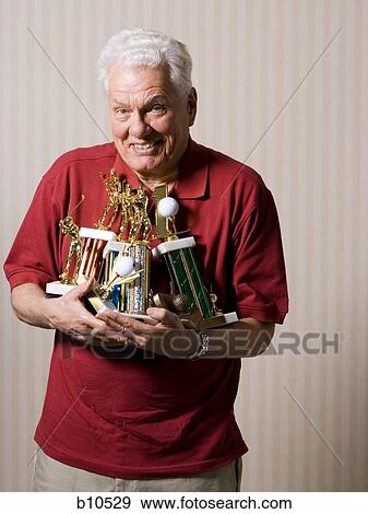 Stock Photo - Portrait of a senior man holding trophies. Fotosearch