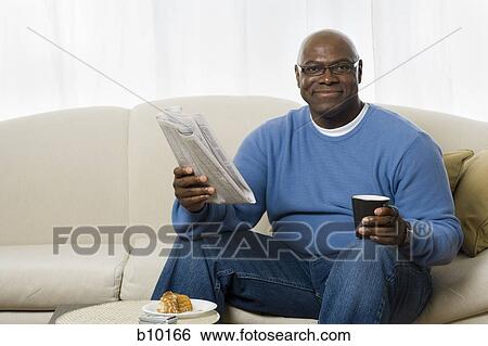 Portrait of a senior man sitting on a couch and holding a tea cup and a newspaper View Large Photo Image Stock Photograph - Portrait of a senior man sitting on a couch and holding a tea cup and a newspaper. Fotosearch