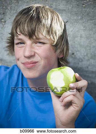 Stock Photograph - Portrait of a teenage boy eating an apple and smiling. Fotosearch