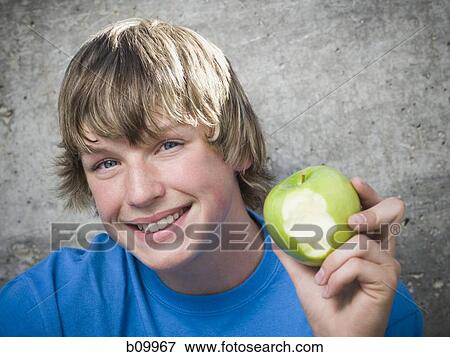 Portrait of a teenage boy holding an apple and looking cheerful View Large Photo Image Stock Photo - Portrait of a teenage boy holding an apple and looking cheerful. Fotosearch