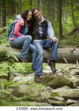 Portrait of a young couple sitting on a fallen tree View Large Photo Image Stock Image - Portrait of a young couple sitting on a fallen tree. Fotosearch