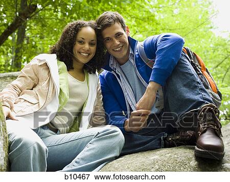 Portrait of a young couple sitting on a rock and smiling View Large Photo Image Stock Photo - Portrait of a young couple sitting on a rock and smiling. Fotosearch