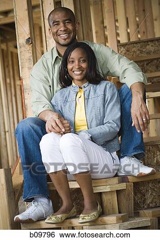 Stock Photograph - Portrait of a young couple sitting on a staircase and smiling. Fotosearch
