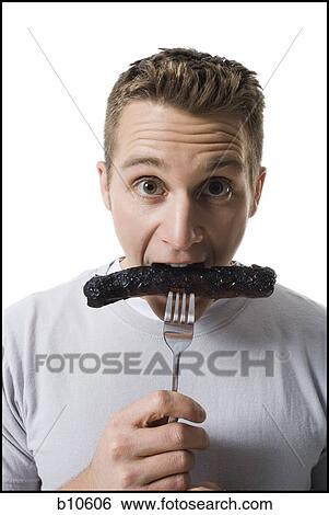Stock Photograph - Portrait of a young man eating a sausage. Fotosearch