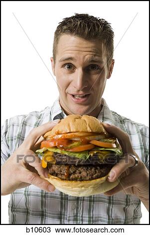 Stock Image - Portrait of a young man holding a hamburger. Fotosearch