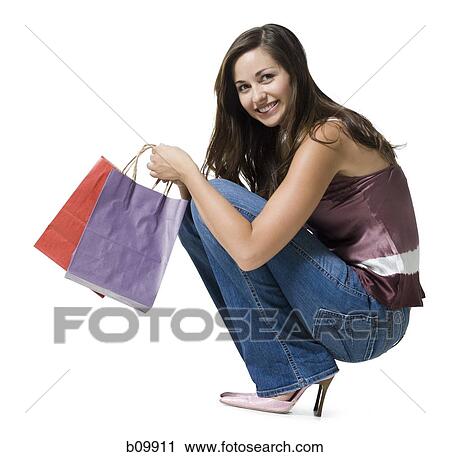 Portrait of a young woman crouching and holding shopping bags View Large Photo Image Stock Image - Portrait of a young woman crouching and holding shopping bags. Fotosearch