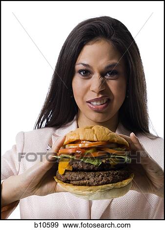 Portrait of a young woman holding a hamburger and making a face View Large Photo Image Stock Photo - Portrait of a young woman holding a hamburger and making a face. Fotosearch