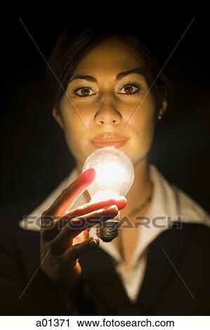 Stock Image - Portrait of a younger businesswoman with illuminated light bulb. Fotosearch
