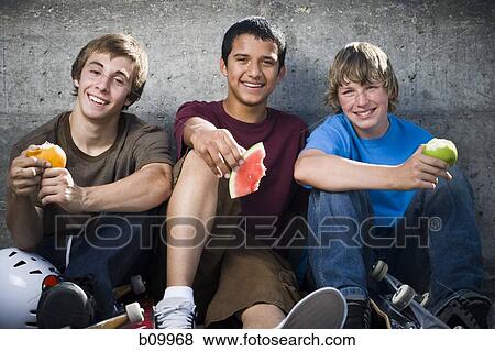 Stock Photo - Portrait of three teenage boys eating fruit. Fotosearch