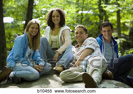 Portrait of two young women and two young men sitting on a rock and smiling View Large Photo Image Stock Photography - Portrait of two young women and two young men sitting on a rock and smiling. Fotosearch