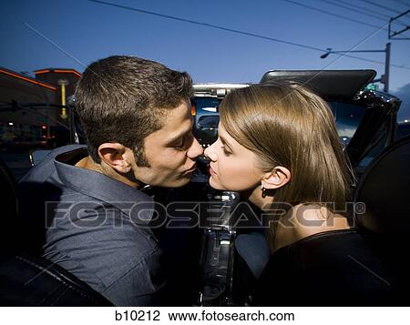Stock Image - Profile of a young couple sitting in a car and kissing. Fotosearch