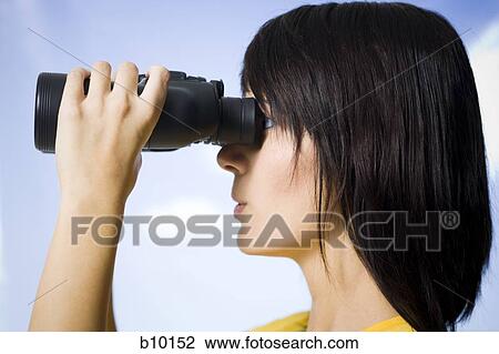 Stock Image - Profile of a young woman looking through a pair of binoculars. Fotosearch