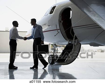 Stock Photography - Profile of two businessmen shaking hands by an airplane. Fotosearch
