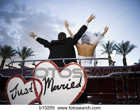 Rear view of a newlywed couple standing in a car with their arms raised View Large Photo Image Stock Photography - Rear view of a newlywed couple standing in a car with their arms raised. Fotosearch