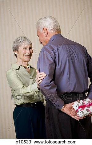 Rear view of a senior man holding a gift with a senior woman looking at him View Large Photo Image Stock Image - Rear view of a senior man holding a gift with a senior woman looking at him. Fotosearch