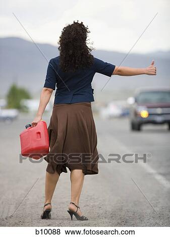 Stock Photo - Rear view of a young woman holding a gas can and hitchhiking. Fotosearch