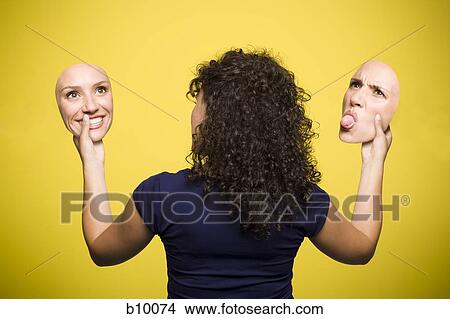 Rear view of a young woman holding cutouts of her face with two different expressions View Large Photo Image Picture - Rear view of a young woman holding cutouts of her face with two different expressions. Fotosearch