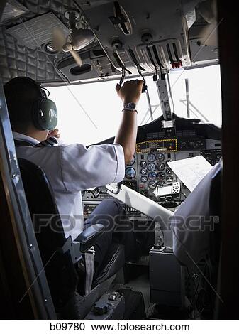 Stock Image - Rear view of two pilots sitting in airplane cockpit. Fotosearch