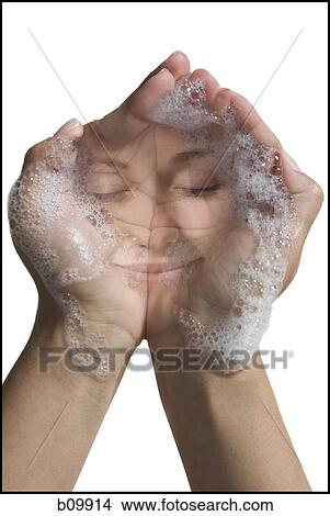 Picture - Reflection of a young woman's face in soap suds in her hands. Fotosearch