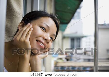 Smiling woman looking out a window View Large Photo Image Stock Photo - Smiling woman looking out a window. Fotosearch