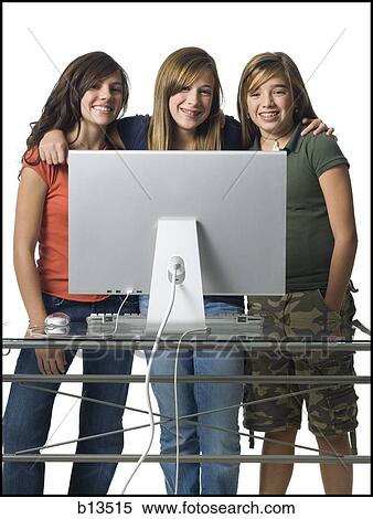Stock Photography - Three girls standing behind computer monitor smiling. Fotosearch