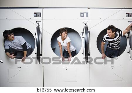 Stock Photography - Three people in dryers at Laundromat smiling. Fotosearch