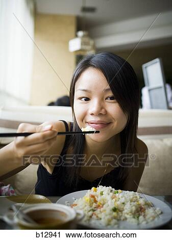 Stock Image - Woman eating at a Chinese food restaurant. Fotosearch