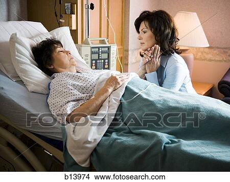 Picture - Woman holding hands with mature woman in hospital bed. Fotosearch