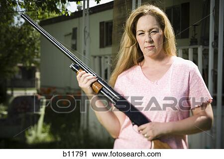 Stock Image - Woman in trailer park with shotgun. Fotosearch