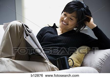Stock Photograph - Woman relaxing on sofa and reading newspaper. Fotosearch