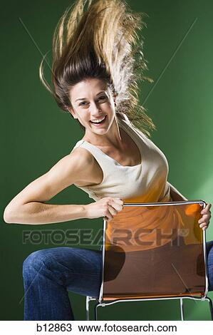 Stock Image - Woman sitting backwards on chair and tossing hair. Fotosearch