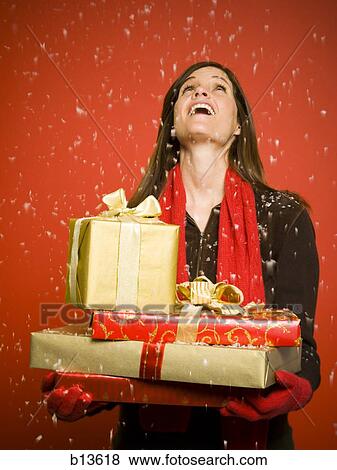 Stock Photo - Woman with Christmas gifts looking up at snow. Fotosearch