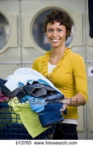 Stock Image - Woman with clothing in laundry basket at Laundromat smiling. Fotosearch