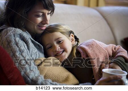 Stock Image - Woman with young girl snuggling on sofa. Fotosearch