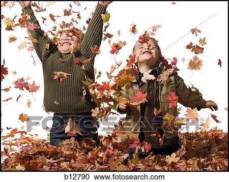 Stock Image - Young children playing in pile of fallen leaves. Fotosearch