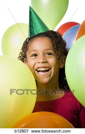 Young girl wearing party hat and playing amongst balloons View Large Photo Image Stock Photo - Young girl wearing party hat and playing amongst balloons. Fotosearch