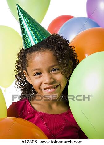 Stock Photograph - Young girl wearing party hat and playing amongst balloons. Fotosearch